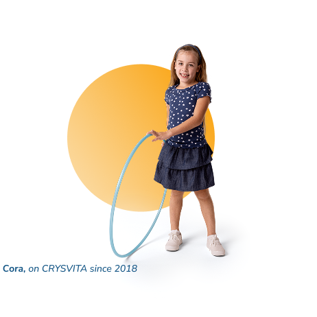 Cora, a person living with XLH, standing and smiling while holding a hula hoop